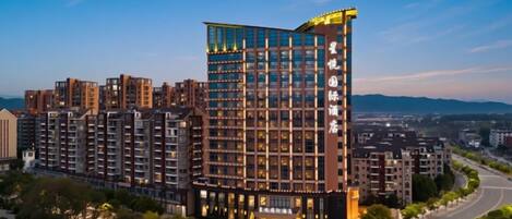 A multi-story hotel with a modern design, featuring a prominent glass facade and a rooftop terrace.