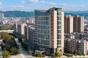 A modern high-rise building with multiple floors, surrounded by a landscaped area with trees and a clear sky. - Xingyue International Hotel (Xianghuli Cultural Creative Ancient Street) (Ganzhou)