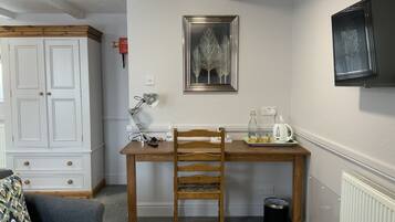 Una habitación con una mesa de madera, una silla, una lámpara de escritorio, un cuadro enmarcado, un armario blanco y un radiador.
