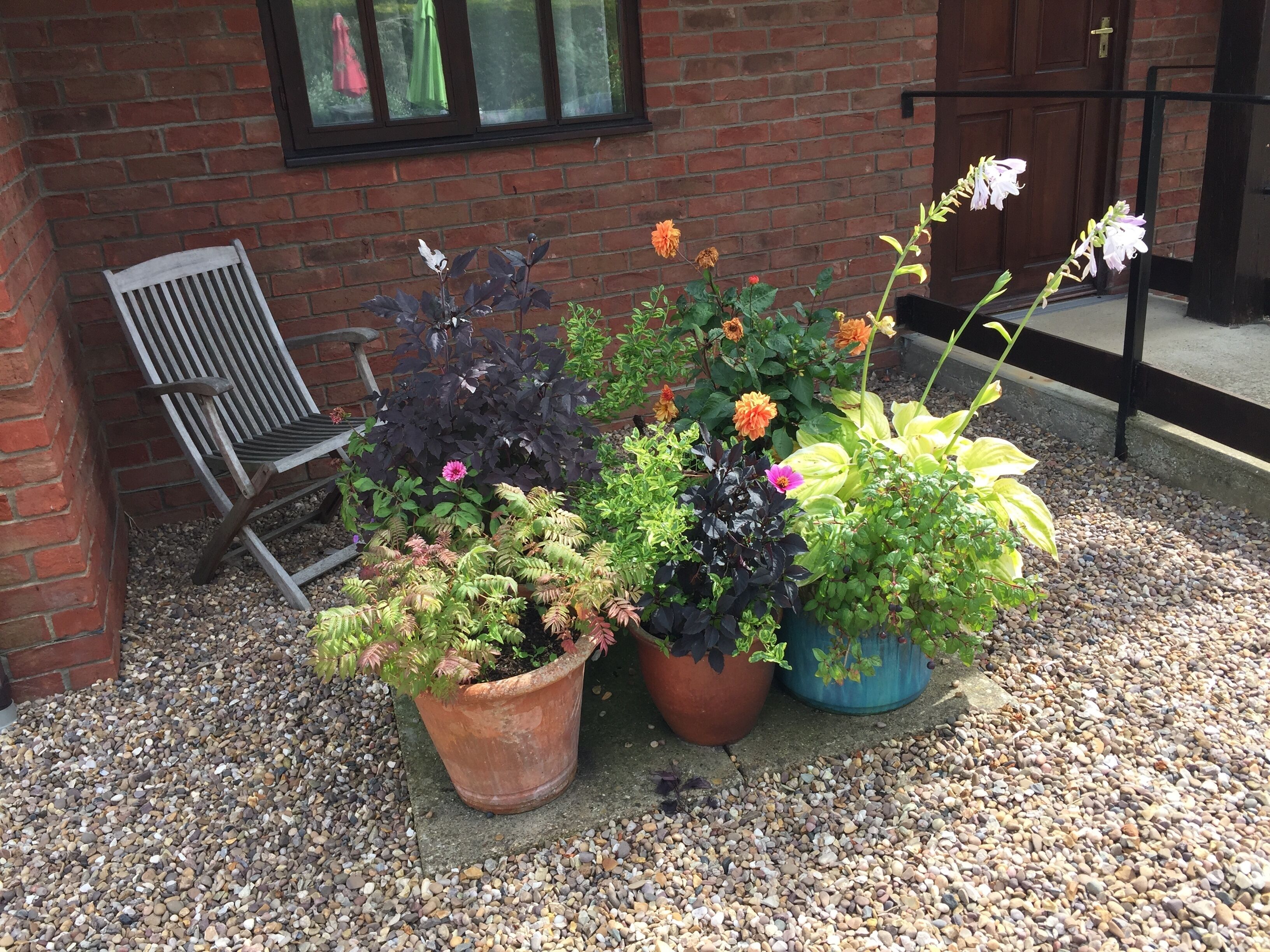 A brick building with a wooden bench and three potted plants with flowers.