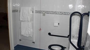 A bathroom with a white toilet, a towel rack, a handrail, and a tiled floor.