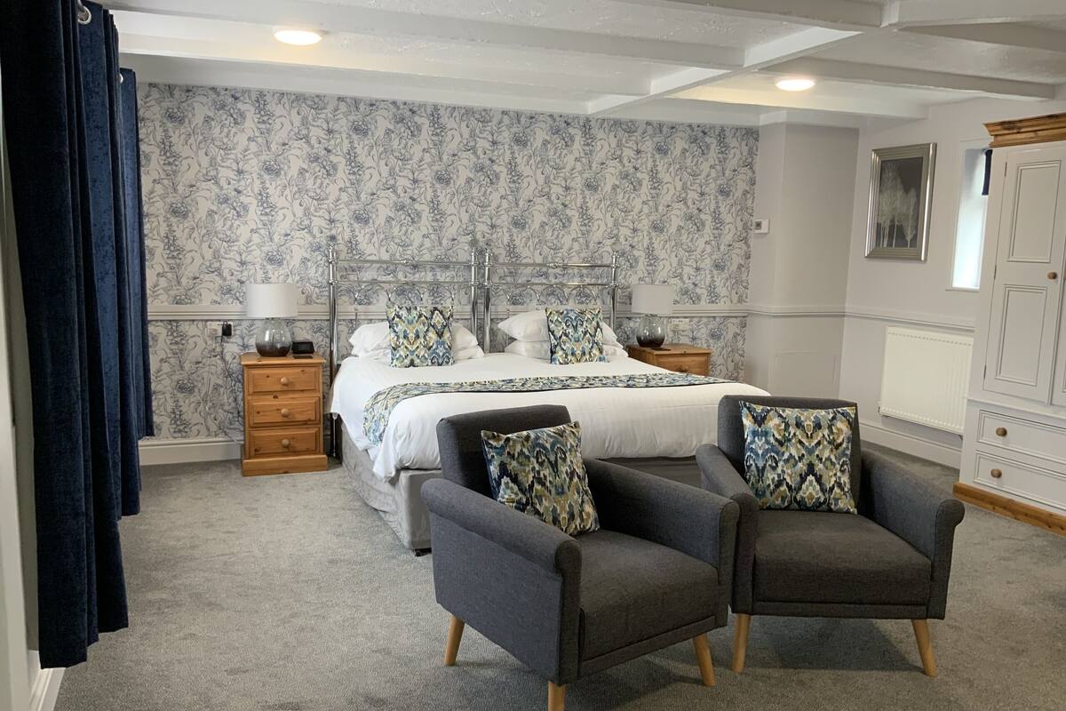 A bedroom with a large bed, two nightstands, a dresser, and two armchairs.