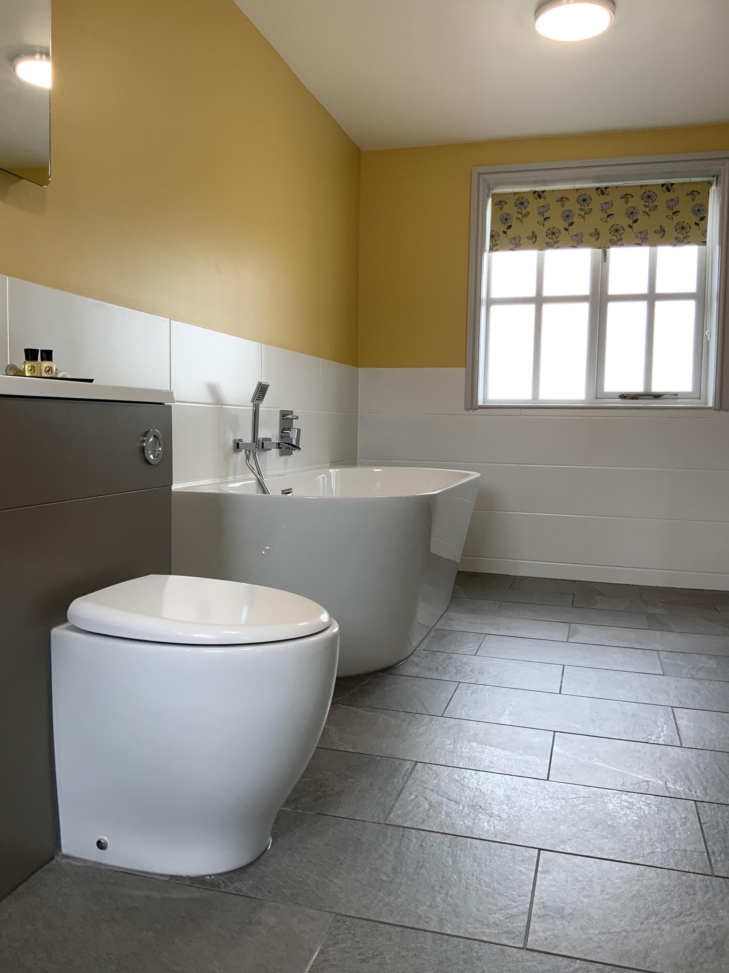 Un baño con inodoro, bañera y ventana con cortina estampada.
