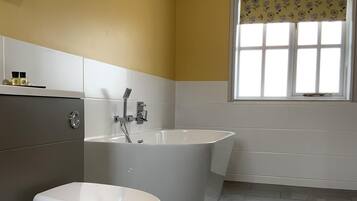Un baño con inodoro, bañera y ventana con cortina estampada.