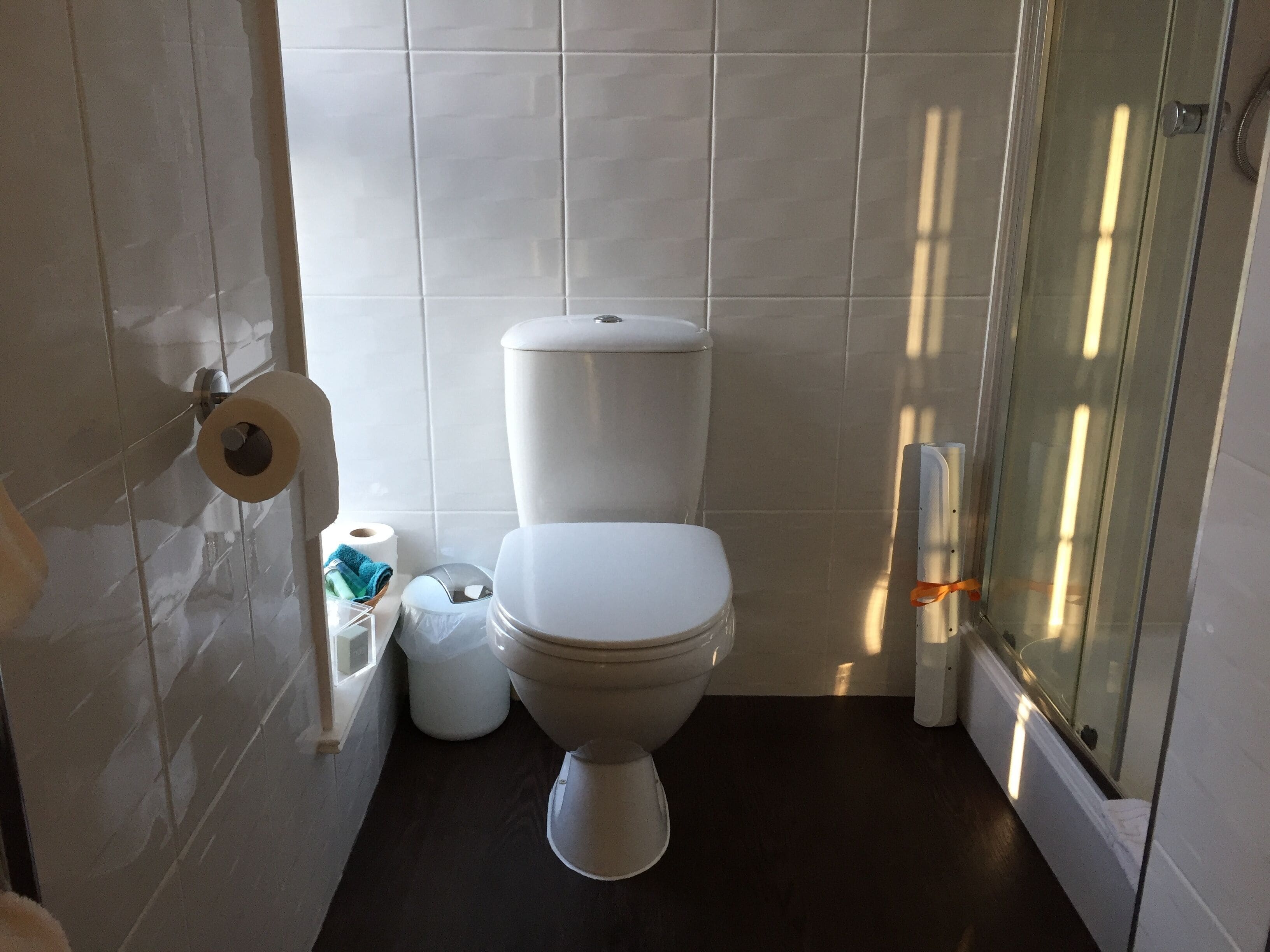 Un baño pequeño y moderno con inodoro, un rollo de papel higiénico, un cesto de basura y zona de ducha.