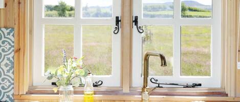 A kitchen with a wooden countertop, a sink, and a window with a view of the countryside.