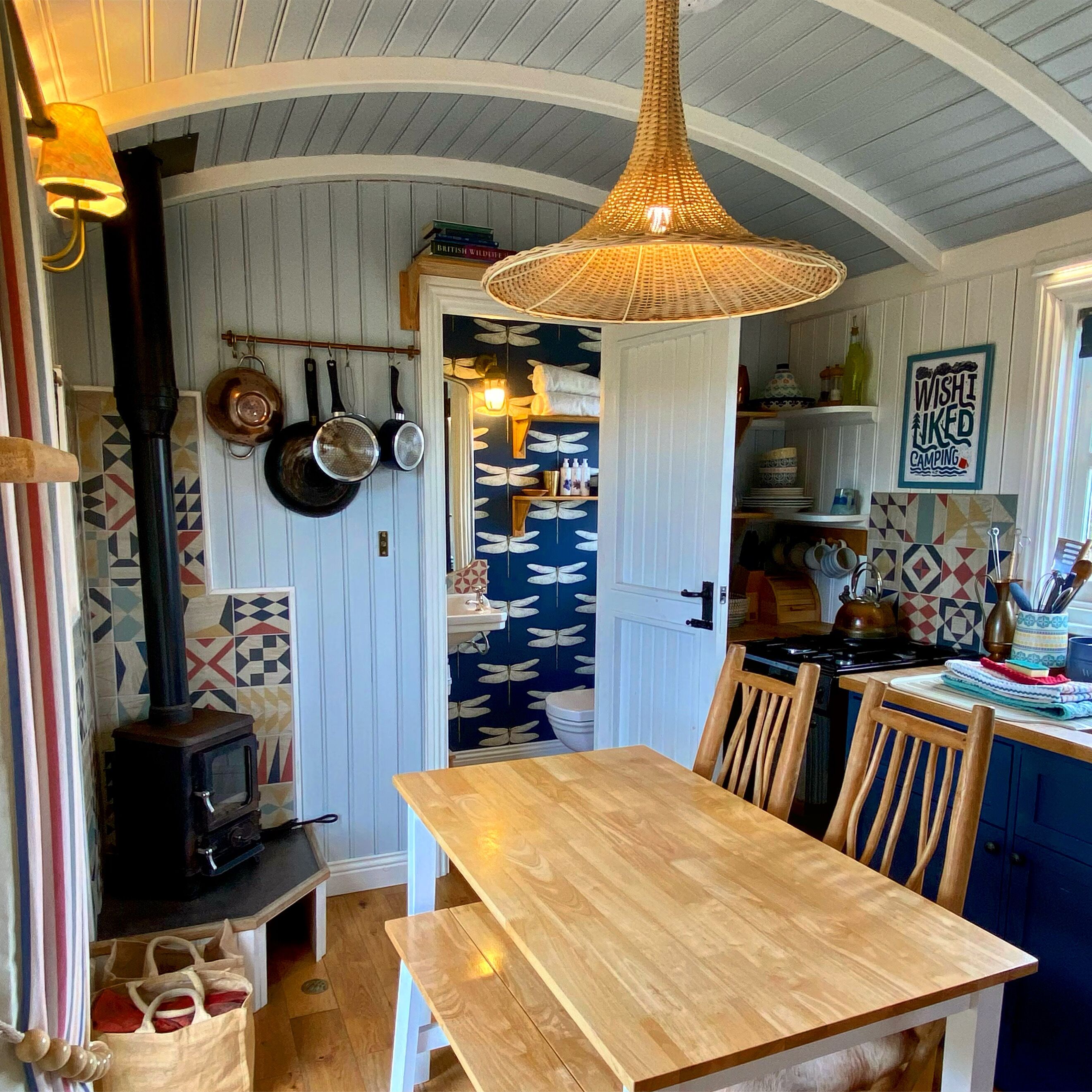 A cozy kitchen with a wooden table, chairs, a hanging pot rack, and a decorative wall with butterfly patterns.