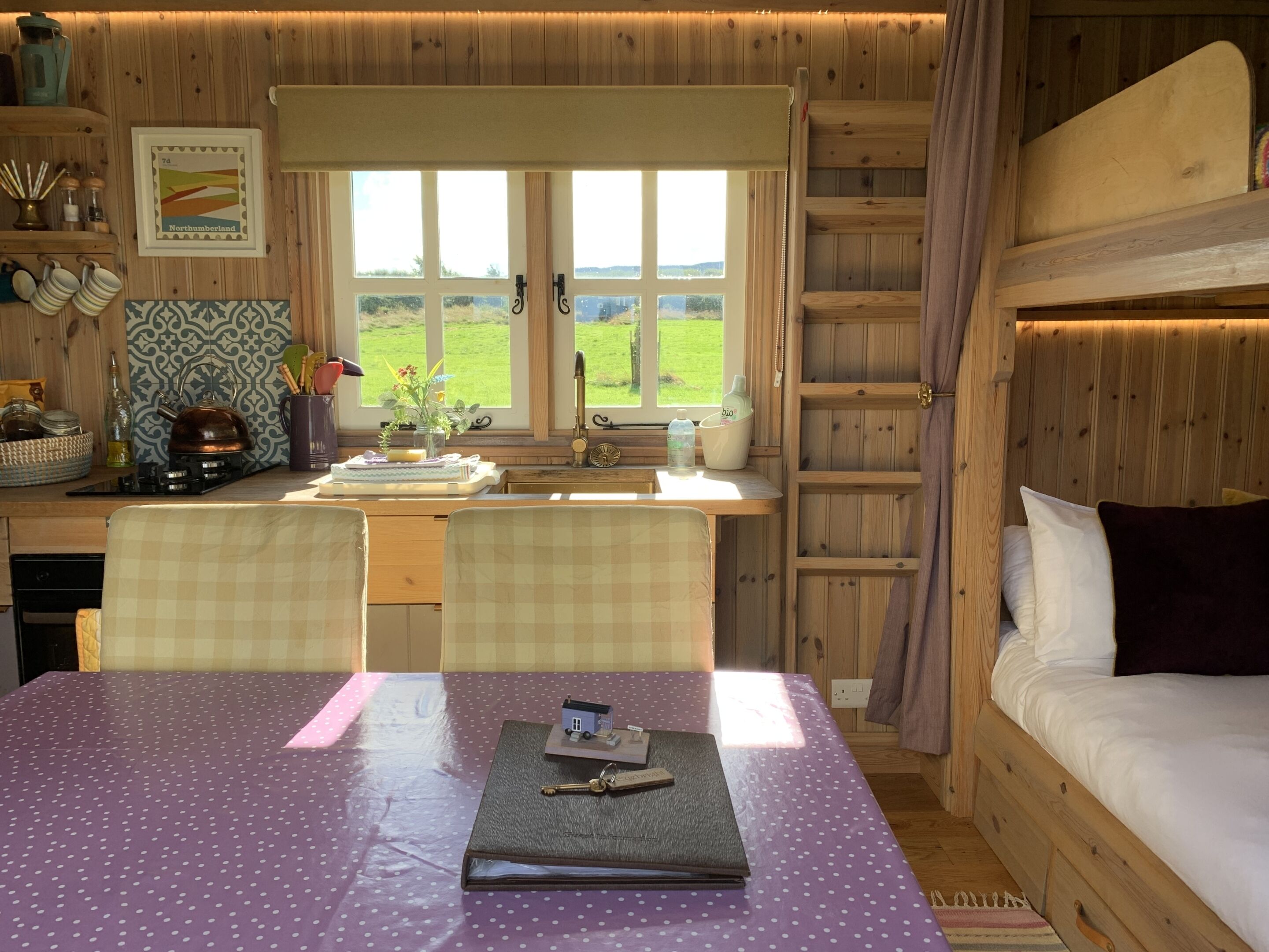 A cozy cabin-style room with a dining table, chairs, a bed, and a window with a view of the countryside.