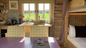 A cozy cabin-style room with a dining table, chairs, a bed, and a window with a view of the countryside.