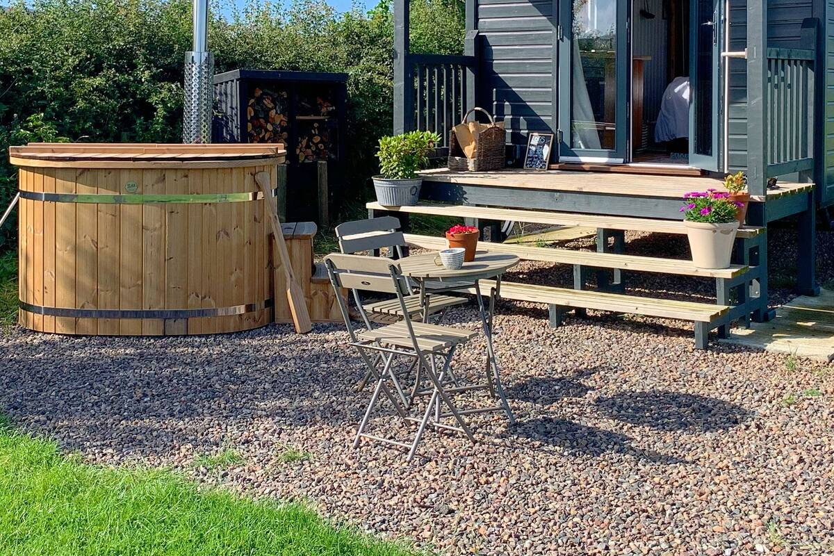 A cozy outdoor seating area with a wooden table and chairs, a hot tub, and a wooden deck.