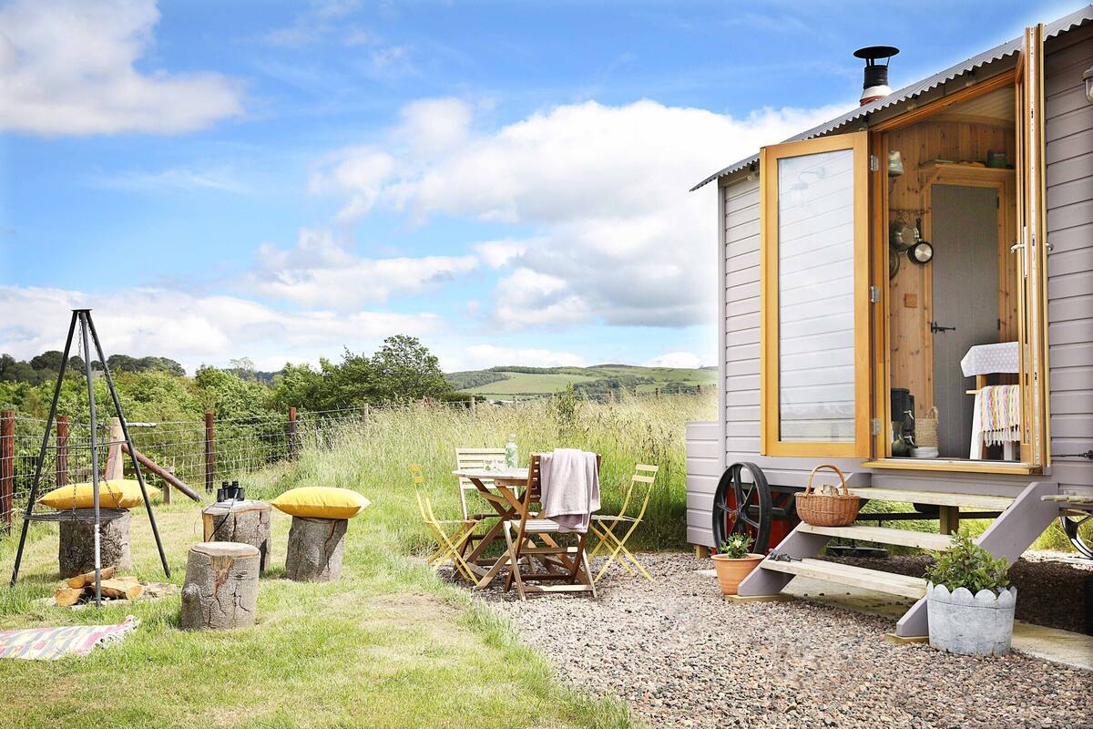 A rustic wooden cabin with a wooden door, a bench, and a table with chairs outside.