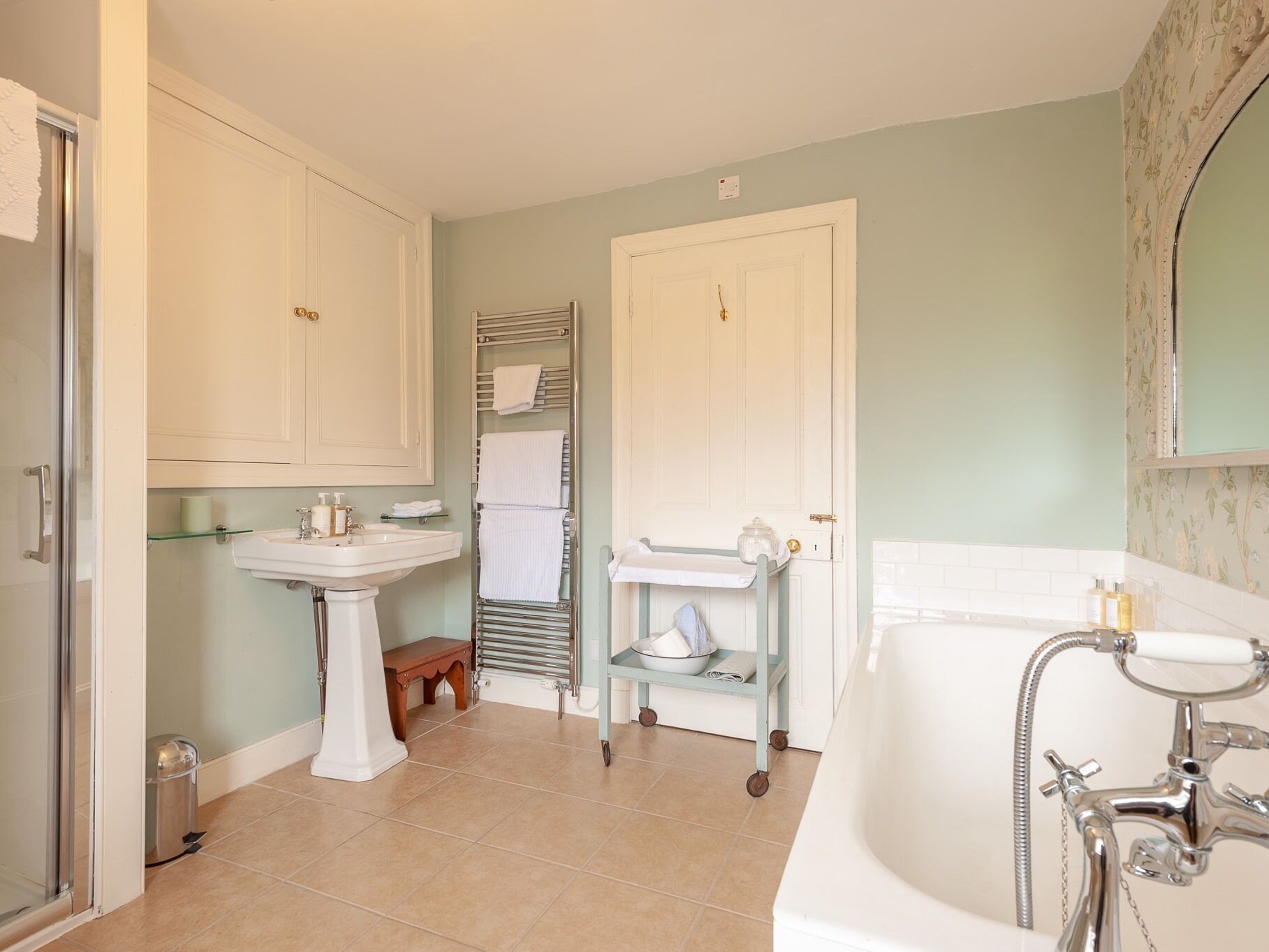 Un baño con bañera, lavabo e inodoro. Hay un perchero y un estante pequeño con artículos de aseo.
