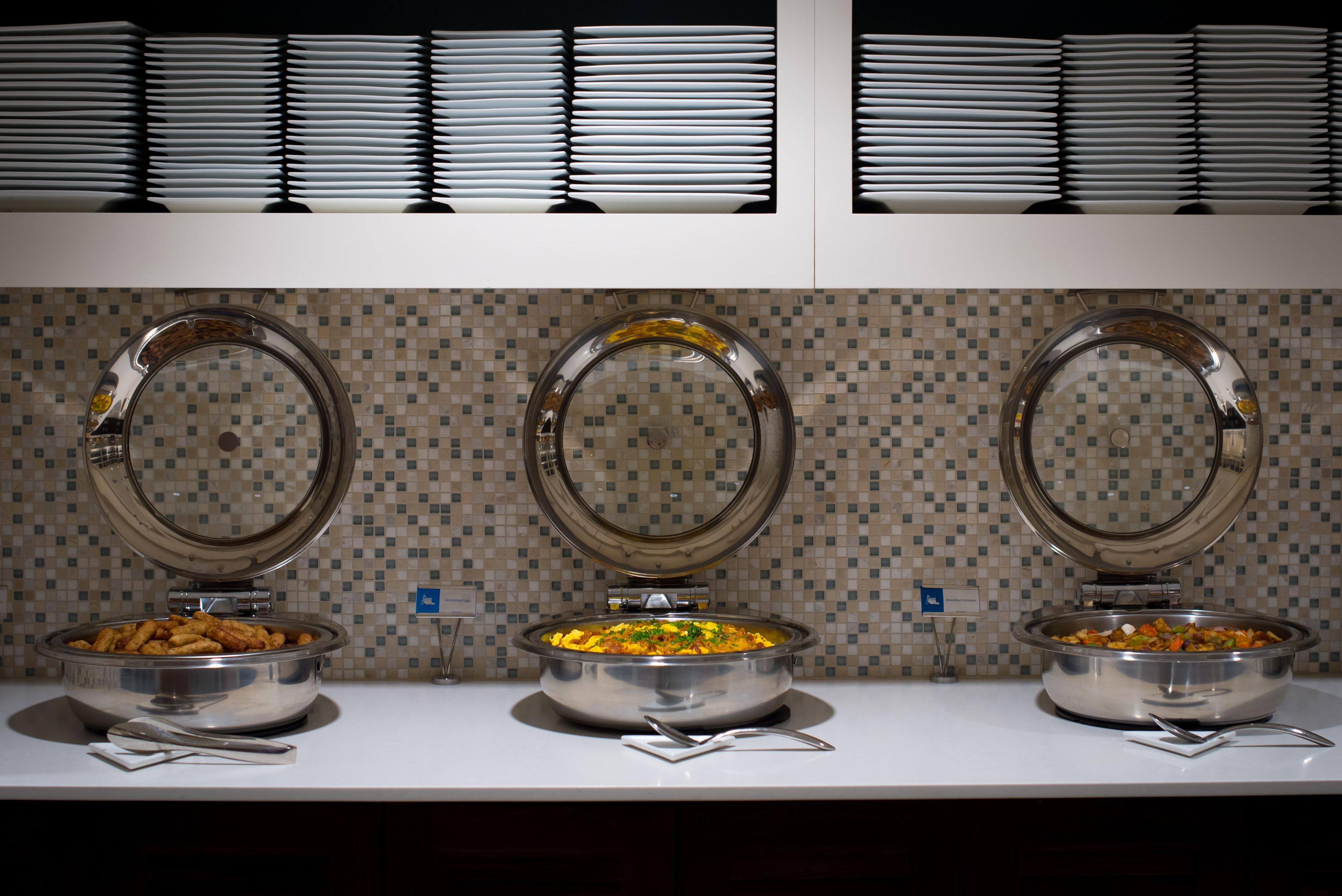 A buffet setup with three bowls of food and a stack of plates.