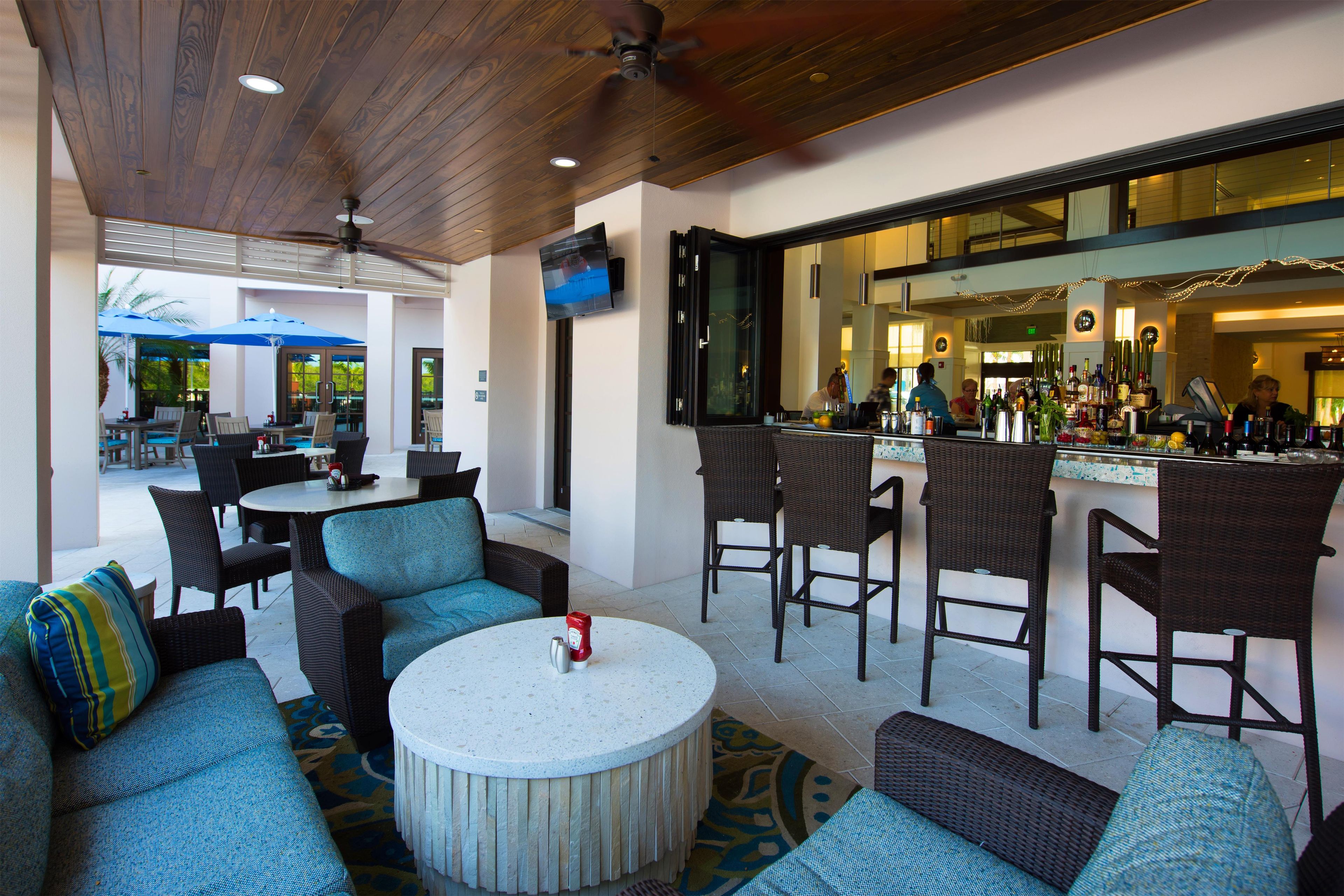 An outdoor seating area with round tables and chairs, a bar with a counter, and a television mounted on the wall.