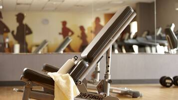 Un gimnasio con equipamiento de ejercicio, incluyendo una banca y pesas, y un espejo que refleja siluetas de personas haciendo ejercicio.