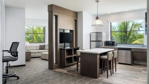 A modern kitchen with a dining area, built-in appliances, and large windows with a view of palm trees. - Hyatt House Naples/5th Avenue (Naples)