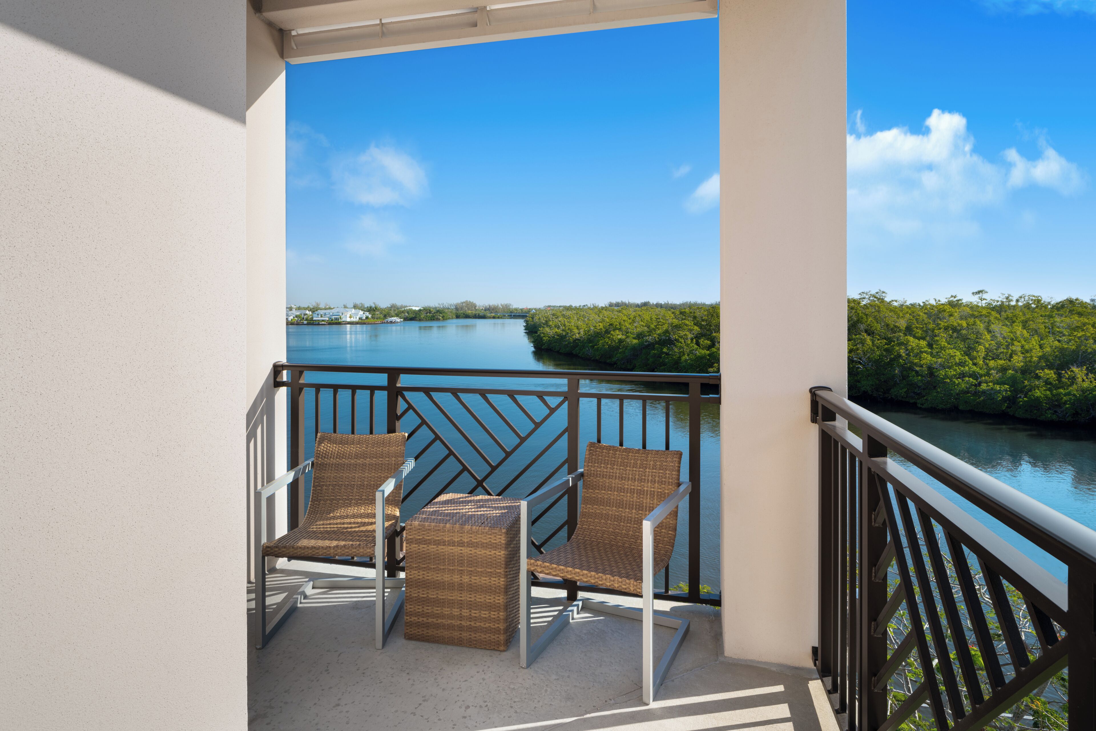 Un balcon agrémenté de fauteuils en osier et d’une petite table, offrant une vue sur une étendue d’eau paisible et une végétation luxuriante.