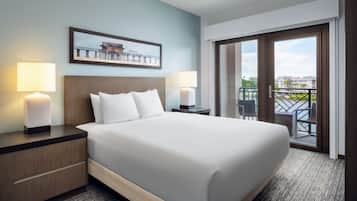 A hotel room with a large bed, two bedside tables with lamps, a view of the outdoors through a sliding door, and a framed picture on the wall.