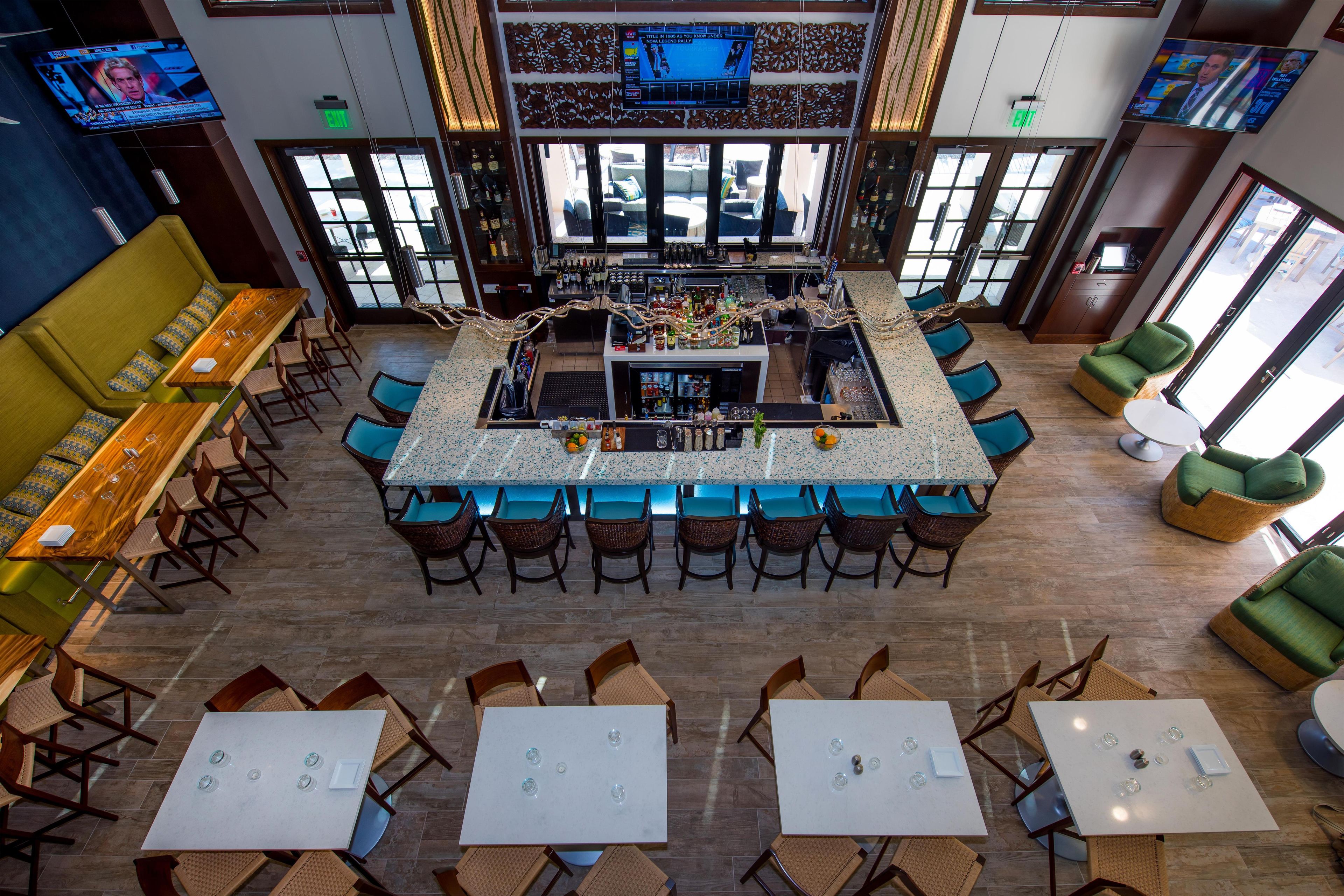 A bar area with a counter, seating around it, and a view of the outside through large windows.