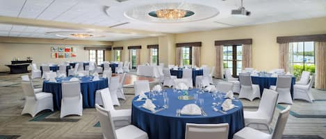 A large conference room with round tables, white chairs, and blue tablecloths.