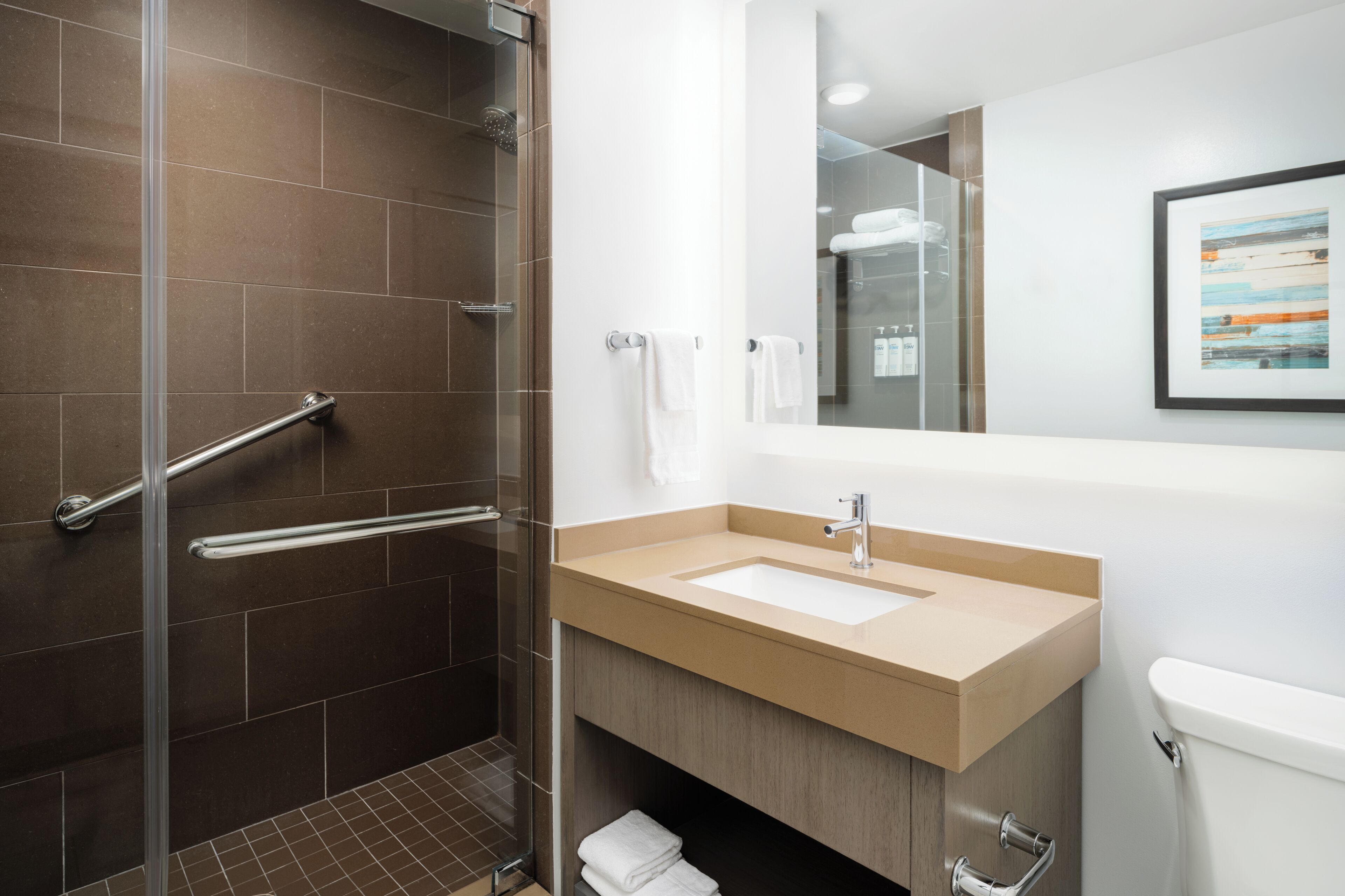 A modern bathroom with a glass shower enclosure, a beige sink, and a white toilet.