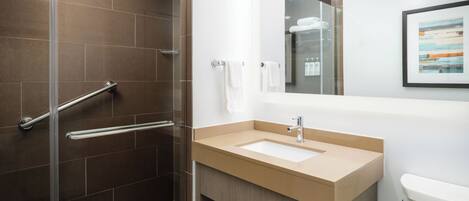 A modern bathroom with a glass shower enclosure, a beige sink, and a white toilet.