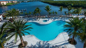 A resort pool with lounge chairs and palm trees, surrounded by a marina and a body of water.