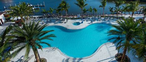 A resort pool with lounge chairs and palm trees, surrounded by a marina and a body of water.