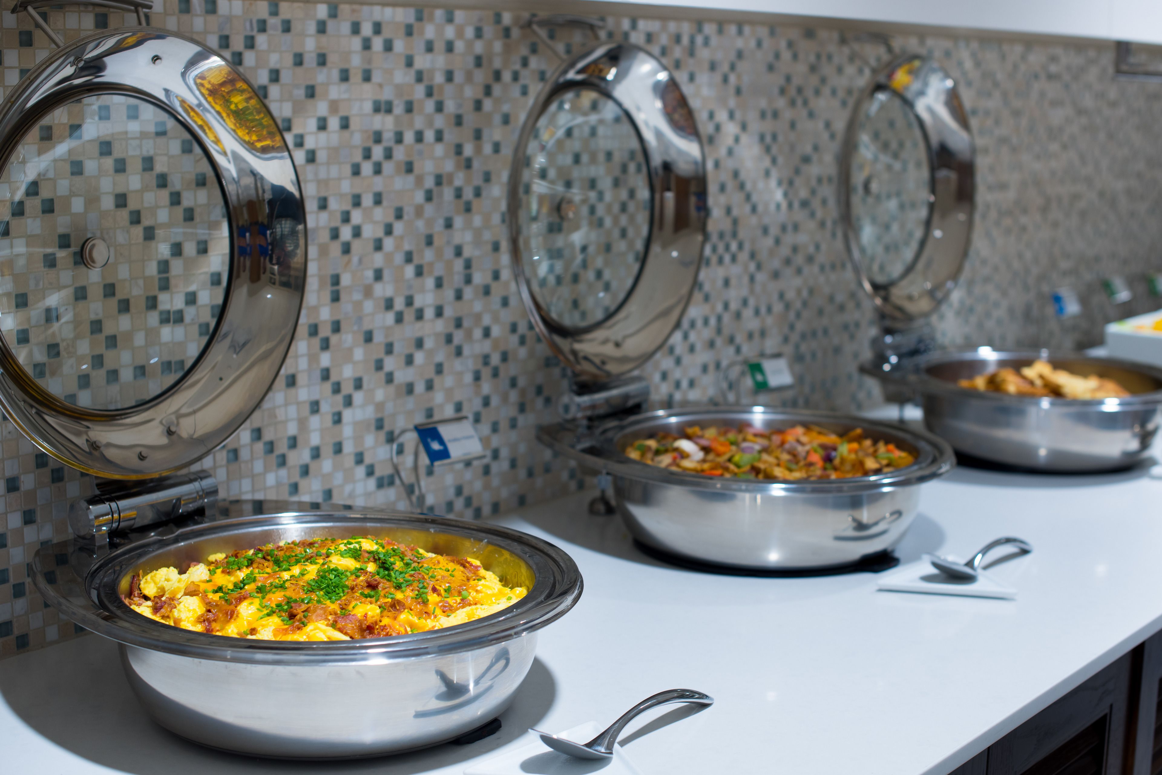 Een buffet met diverse gerechten in roestvrijstalen kommen, elk met een deksel.