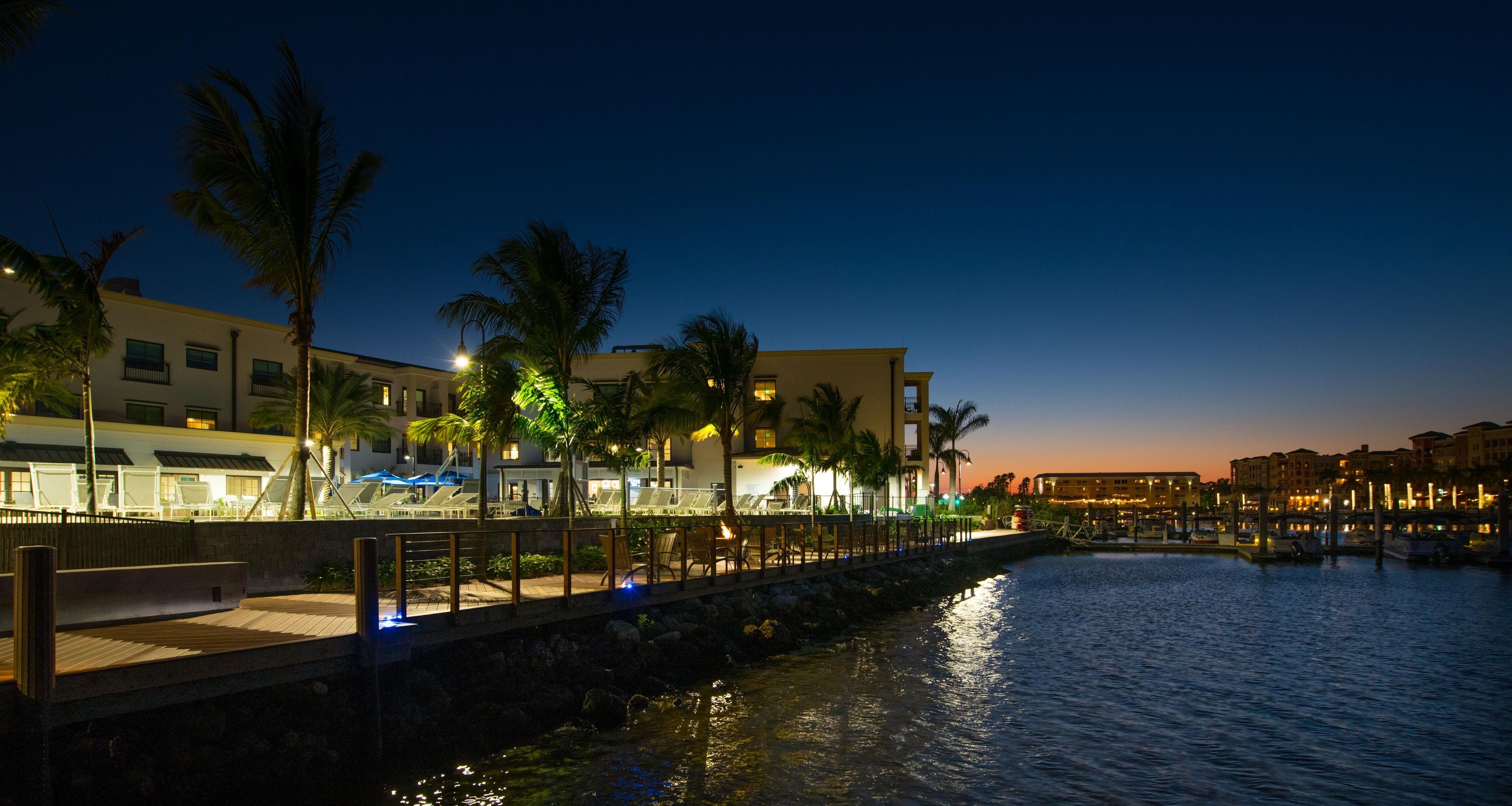 A waterfront hotel with a boardwalk, palm trees, and a sunset view.