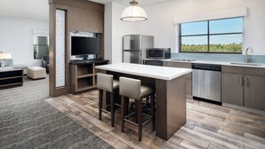 A modern kitchen with a central island, bar stools, a built-in TV, and a large window offering a view. - Hyatt House Naples/5th Avenue (Naples)