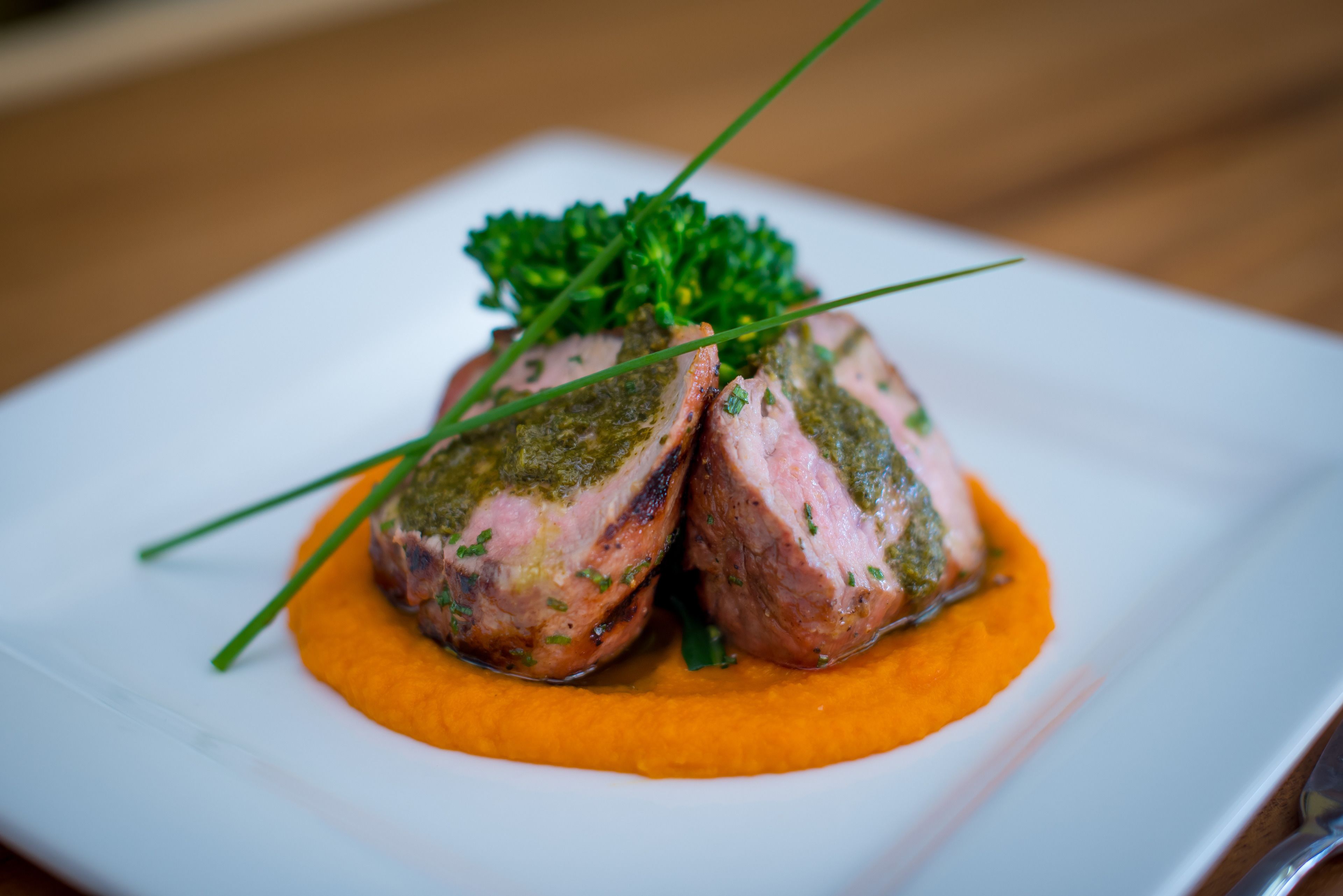 A plate with two pieces of meat topped with green sauce and garnished with chives.