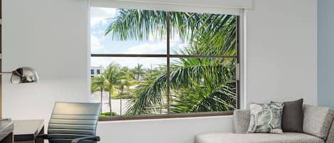 A modern hotel room with a large window offering a view of palm trees and a clear sky.