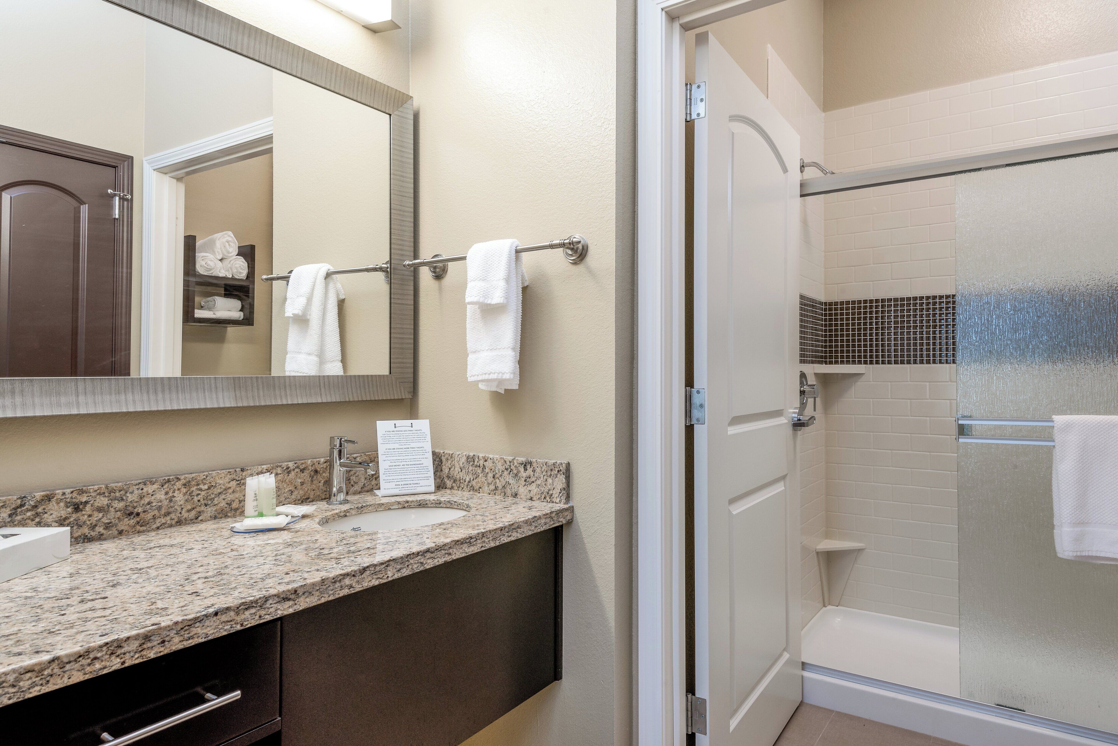 A bathroom with a granite countertop, a sink, a mirror, a towel rack, and a glass-enclosed shower.