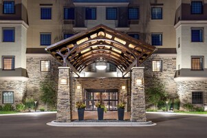 A hotel entrance with a stone facade, multiple windows, and a covered entrance area with potted plants.