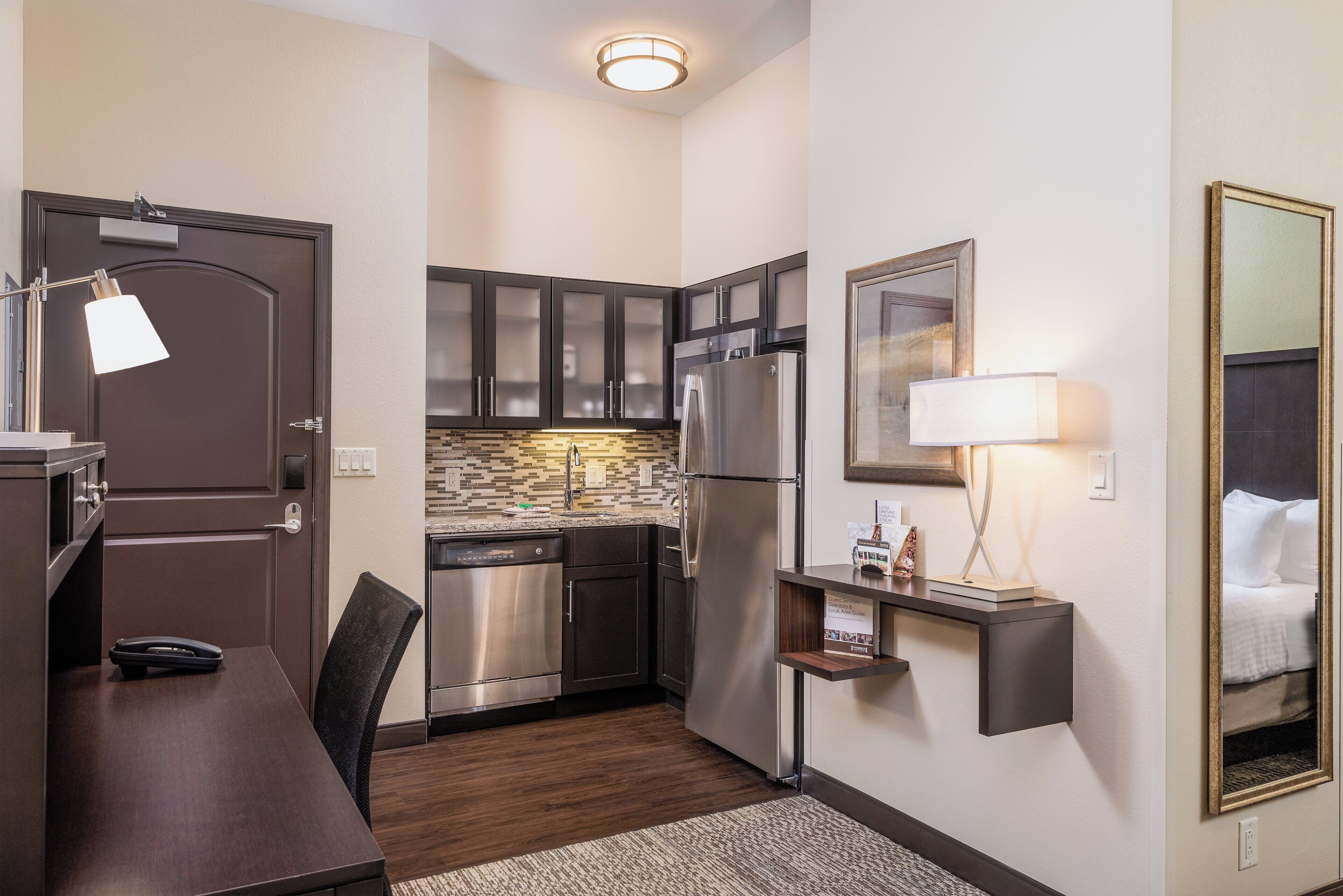 A compact hotel room with a kitchenette, a dining area, and a bed.