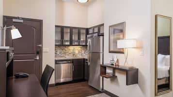 A compact hotel room with a kitchenette, a dining area, and a bed.