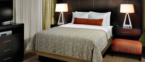 A hotel room with a bed, two bedside tables with lamps, a TV on a dresser, and a carpeted floor.