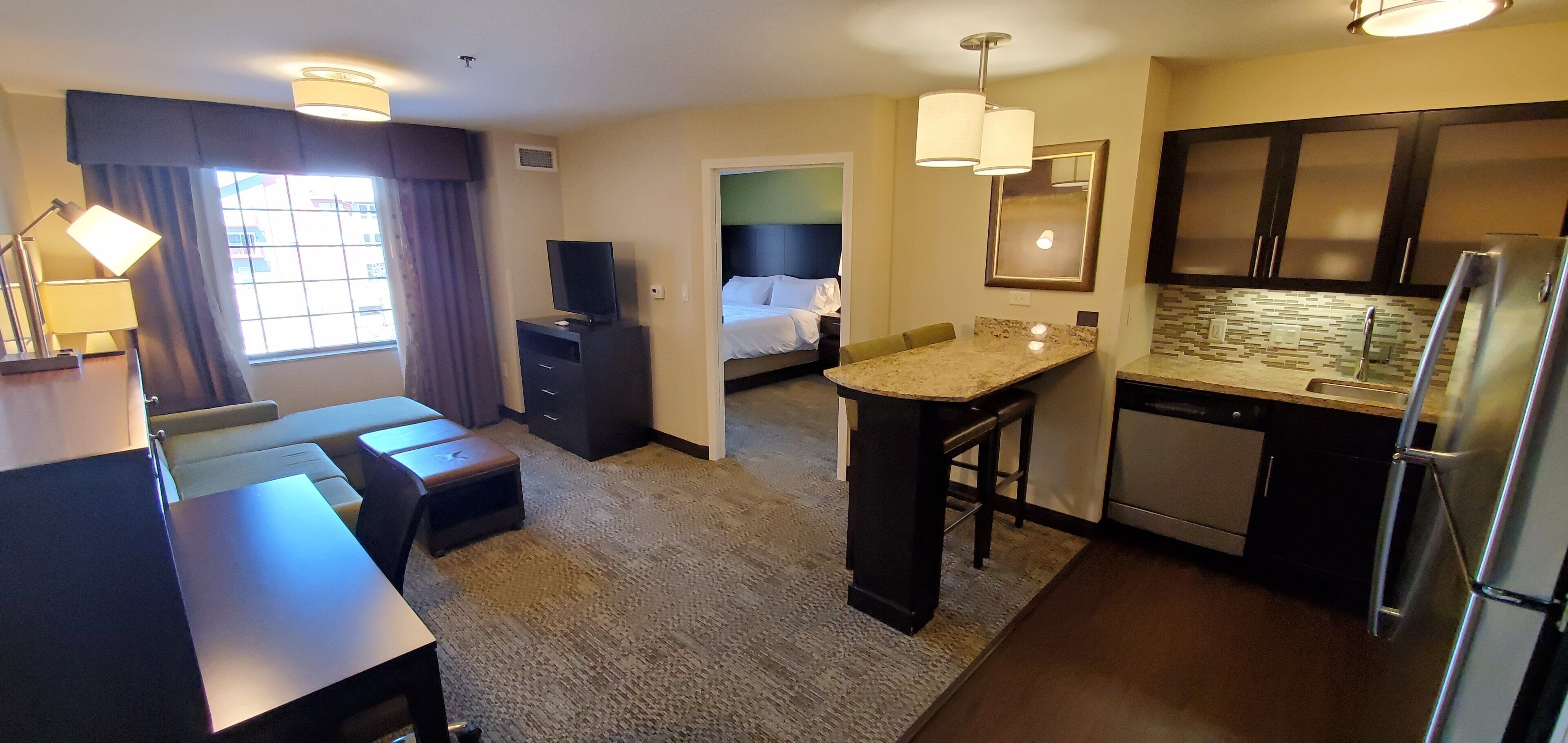 A hotel room with a kitchenette, a bed, a desk, and a TV.