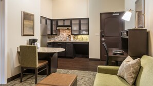 Un espacio habitable compacto con kitchenette, una zona de comedor con una mesa redonda y dos sillas, y un sofá verde con un cojín estampado.