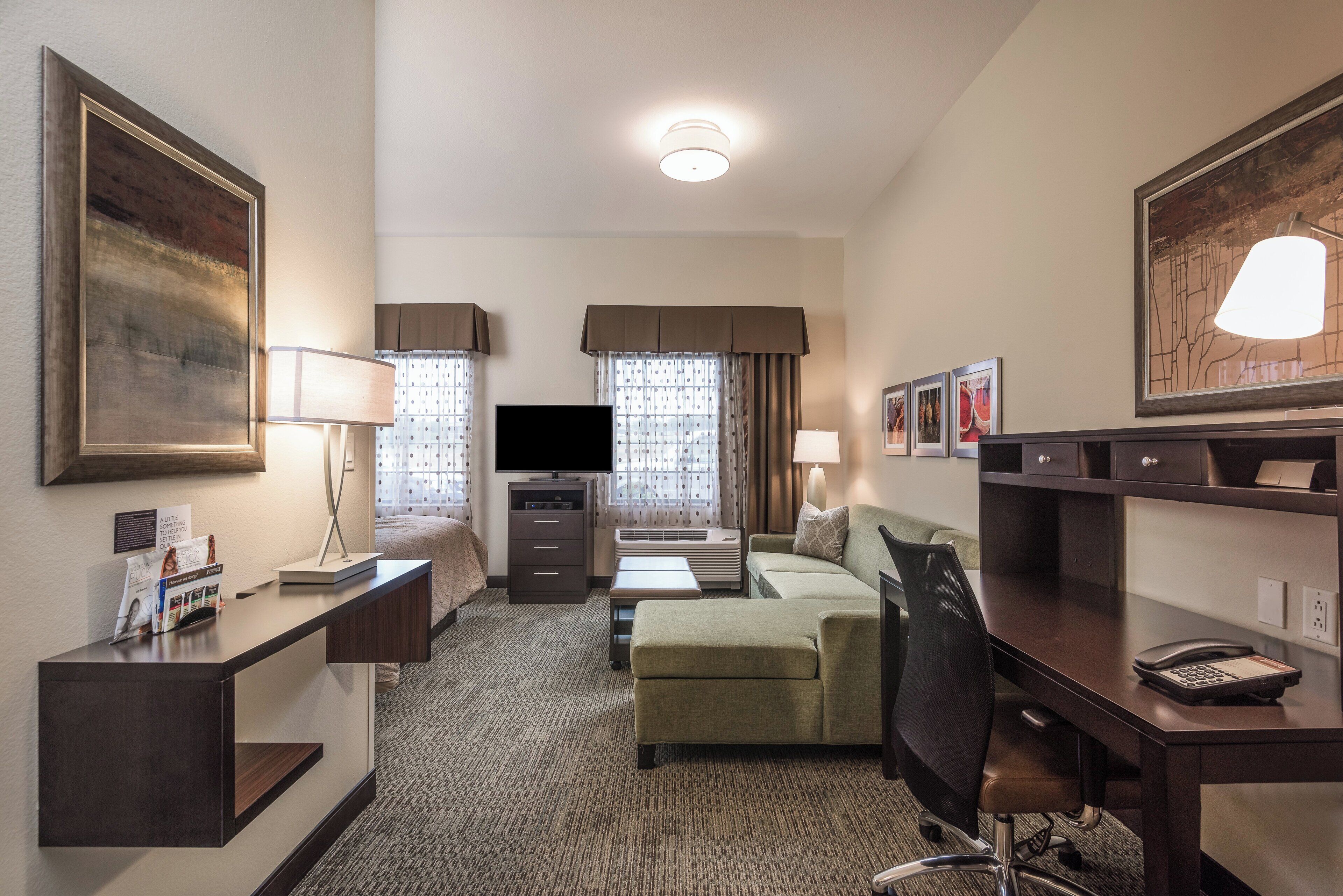 A hotel room with a desk, a sofa, a television, a bed, and a large mirror.