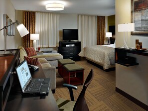 Habitación de hotel con cama, escritorio, laptop, televisor, cómoda y silla.