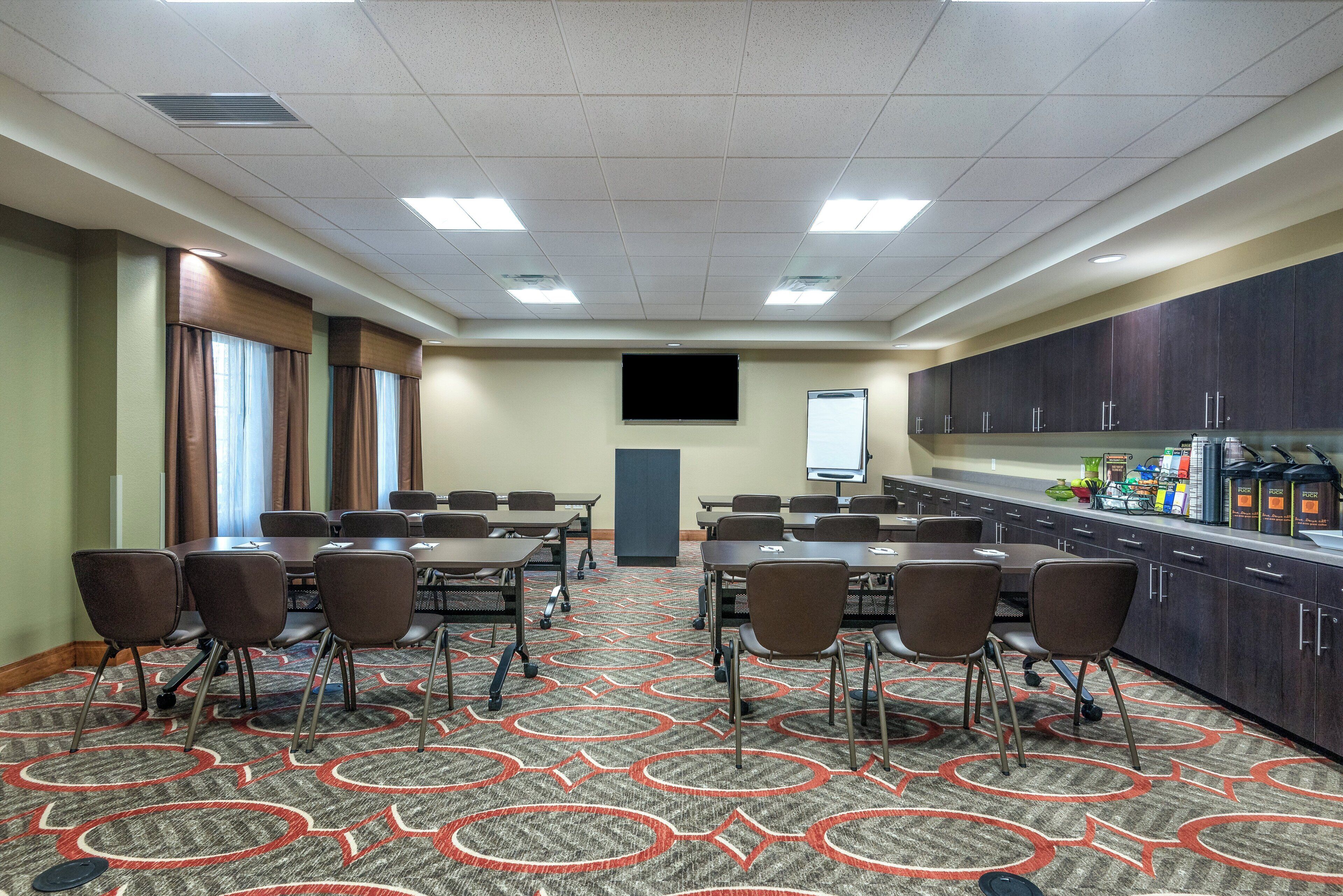 Una sala de conferencias con mesas, sillas, una pantalla de proyector y una kitchenette.