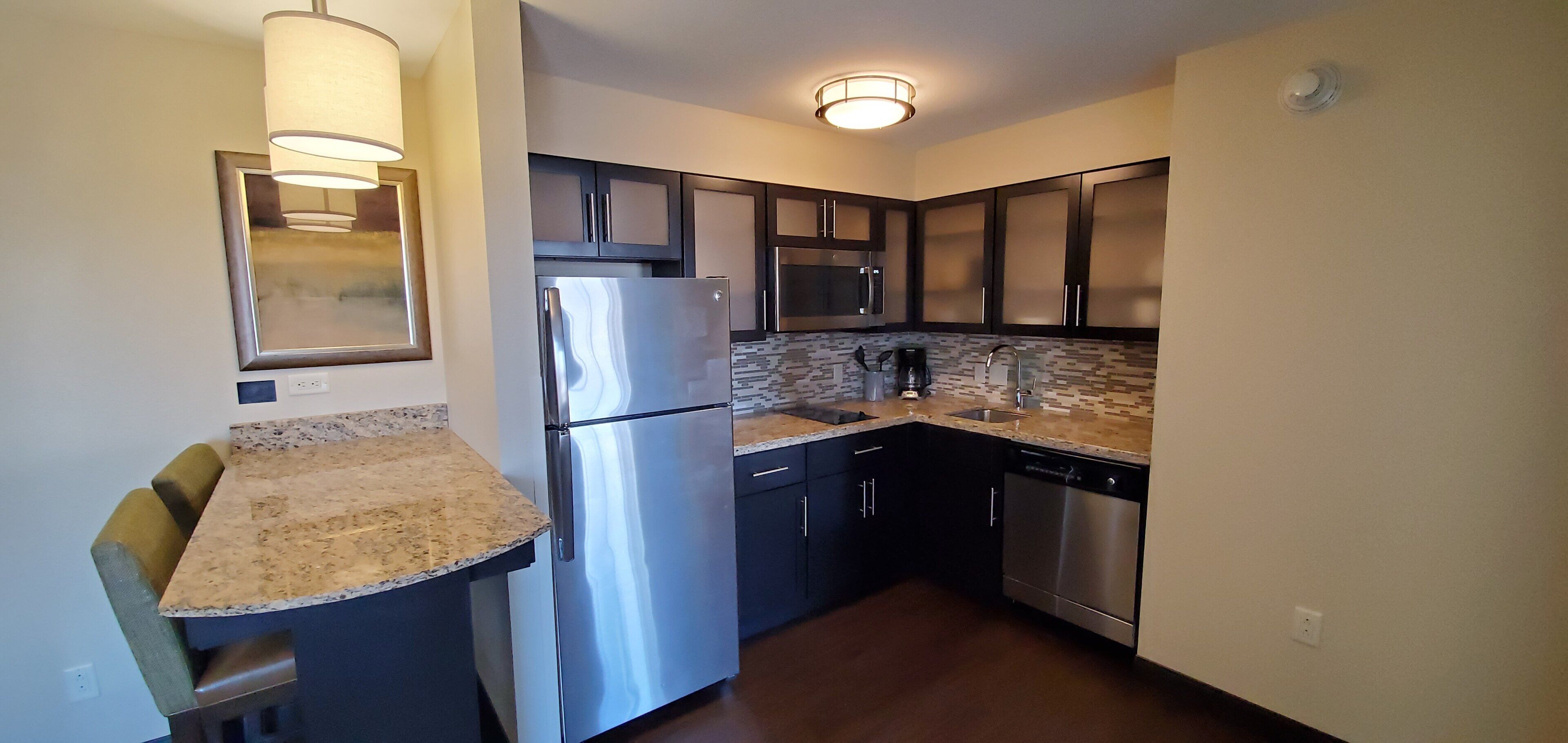 A compact kitchen with a refrigerator, microwave, dishwasher, and a small island with a sink.