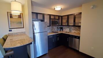 A compact kitchen with a refrigerator, microwave, dishwasher, and a small island with a sink.