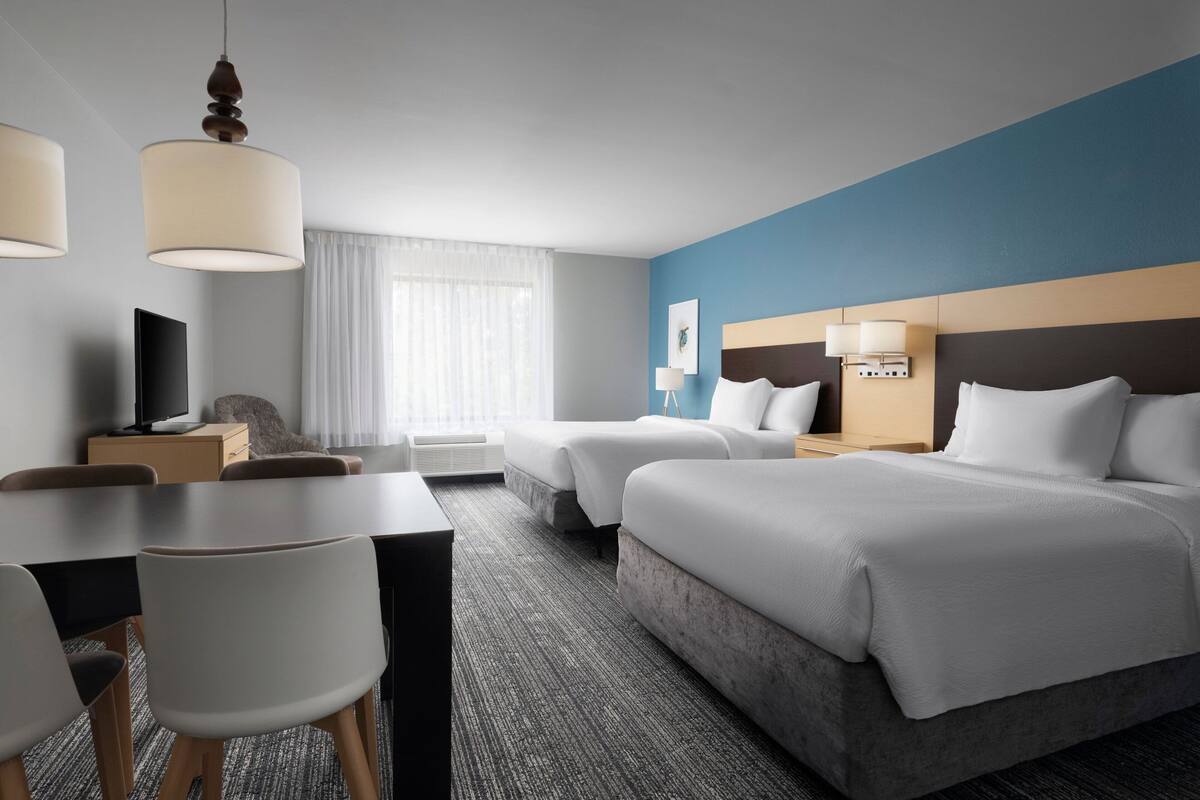 Ein Hotelzimmer mit Bett, Schreibtisch, Stuhl, Fernseher und einem Fenster mit Vorhängen.
