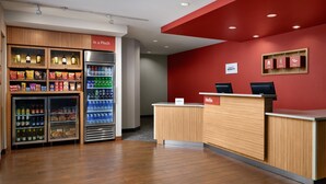A reception area with a red wall, a wooden reception desk, and a refrigerator stocked with beverages and snacks. - Towneplace Suites Columbia Northwest/Harbison (Columbia)
