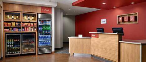 A reception area with a red wall, a wooden reception desk, and a refrigerator stocked with beverages and snacks.