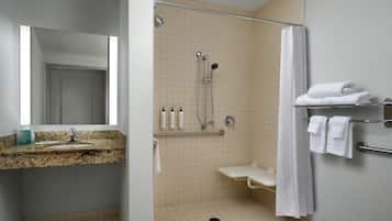 Un baño con encimera de granito, lavamanos, espejo, ducha con puerta de cristal y toallero con toallas dobladas.