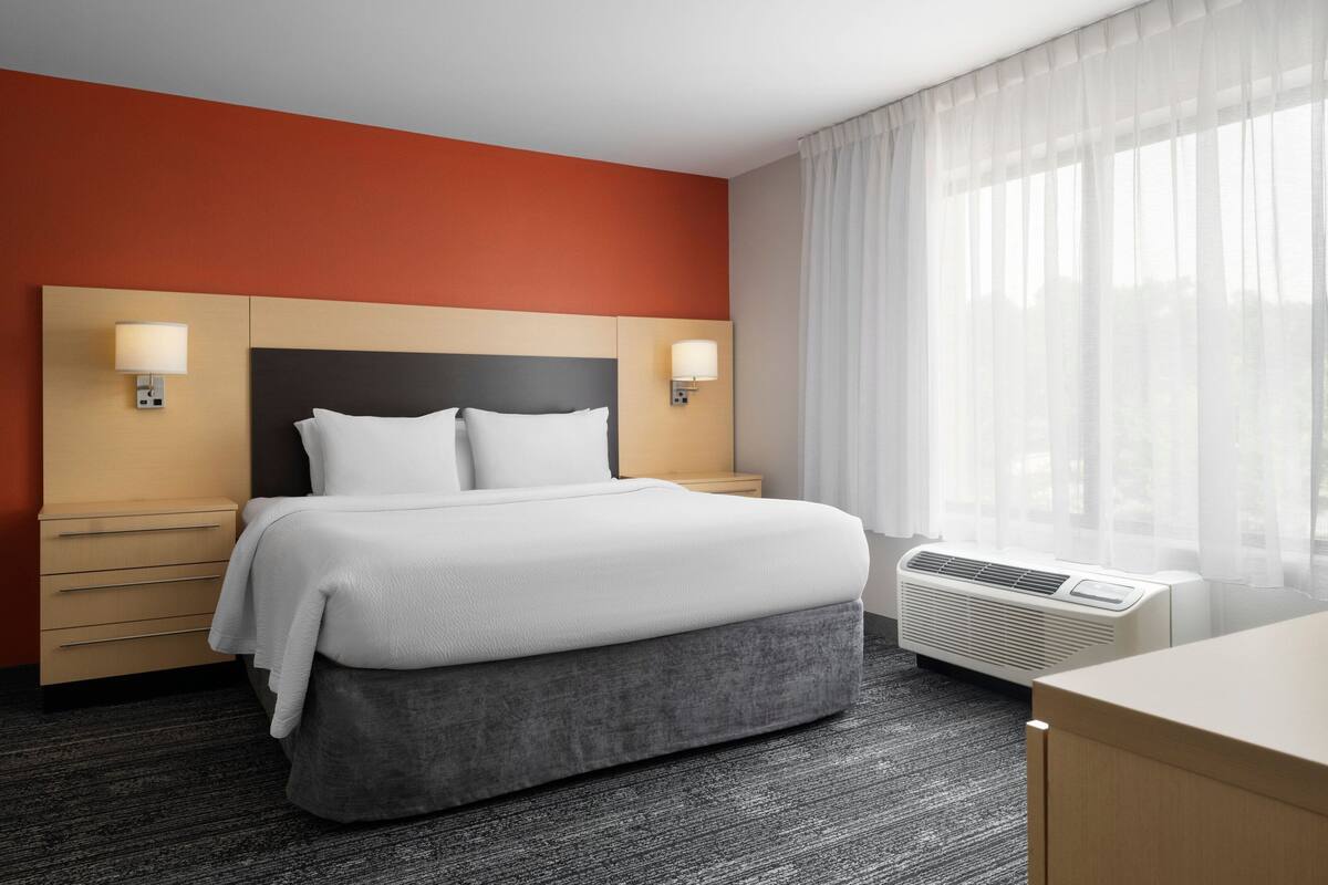 Ein Hotelzimmer mit Bett, Nachttischen, einem Schreibtisch und einem fenster mit Vorhängen.